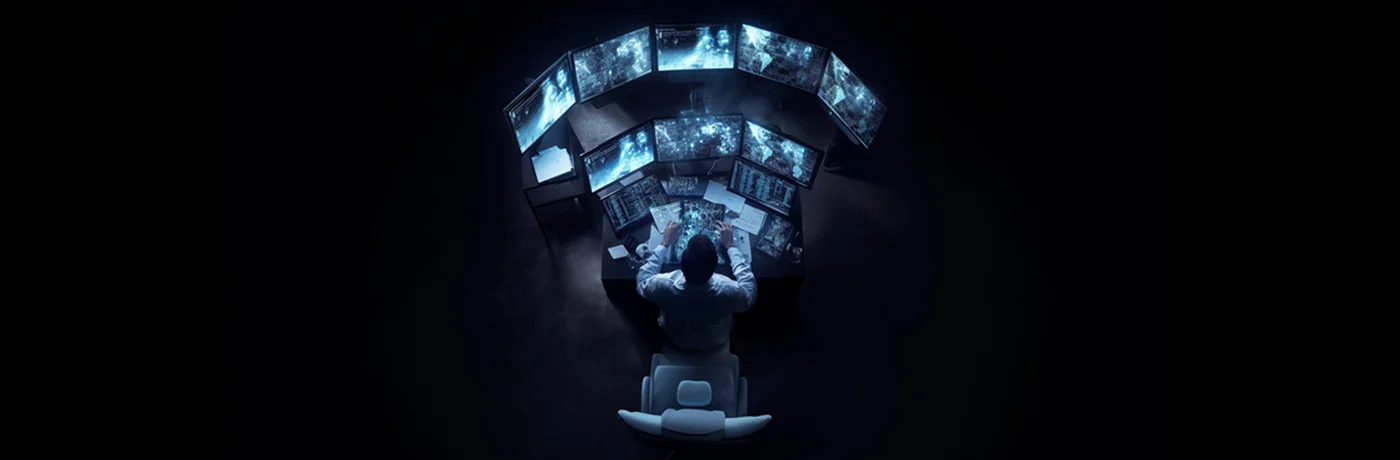 Person analyzing data on multiple monitors in a dark room.